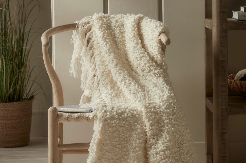 A calm scheme with neutral shades and a designer chair with a boucle throw on top of it.