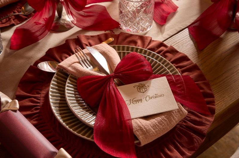A charming and romantic Christmas table scheme with round ruffle place mats, fluted dinner sets, and cutlery tie sup with ribbons.
