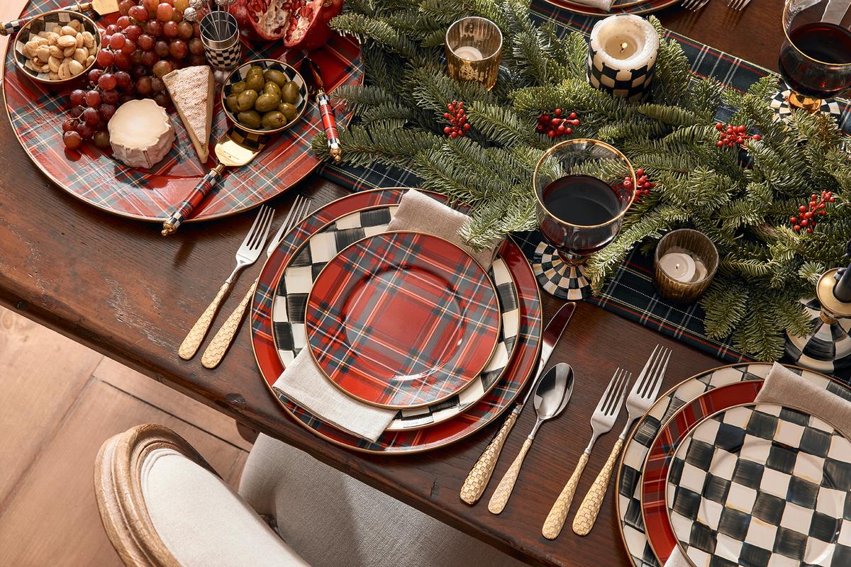 Classic Christmas tablescape with plaid and checkerboard plates, a centrepiece with foliage and gold cutlery.