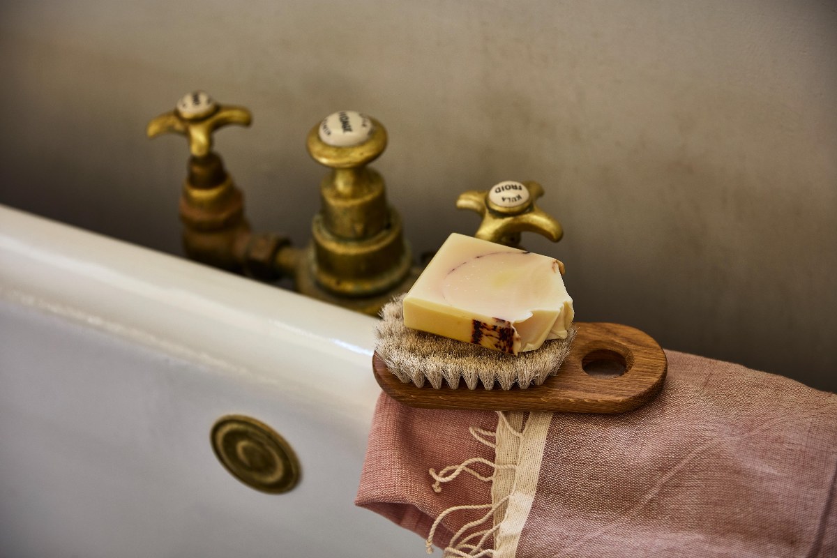 The edge of a bath with a linen towel, soap and body brush.