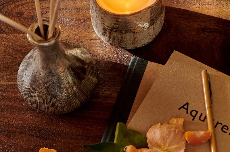 A reed diffuser and candle on a wood bedroom table.