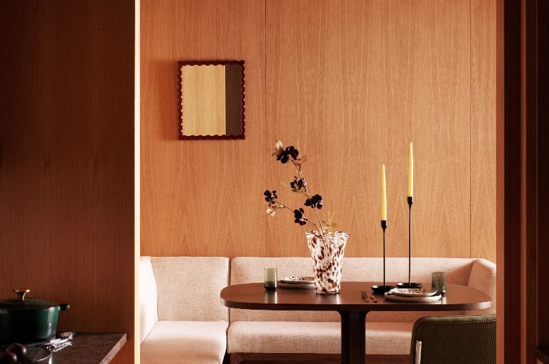 A wood drenched kitchen-diner with an L-shaped banquette, retro chairs, a wood table, and minimalist decor.