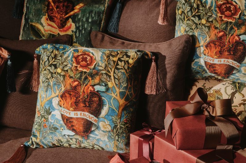 Patterned and soft brown cushions on a brown sofa with red presents wrapped next to them.