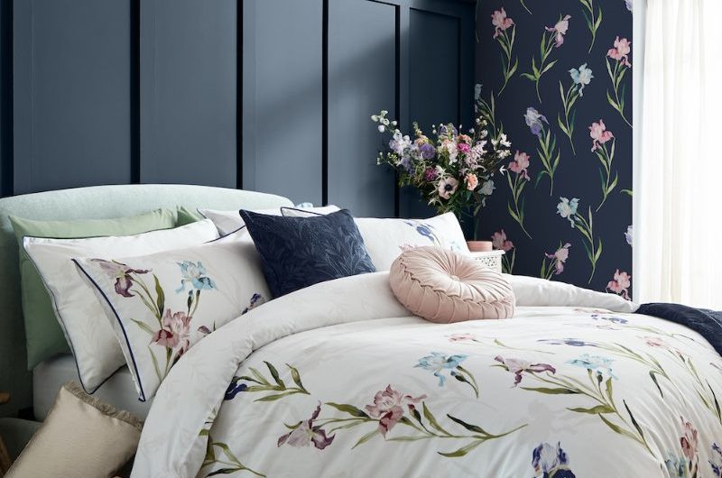 Bedroom design with floral wallcoverings, blue panelling, floral bedding and wood flooring.