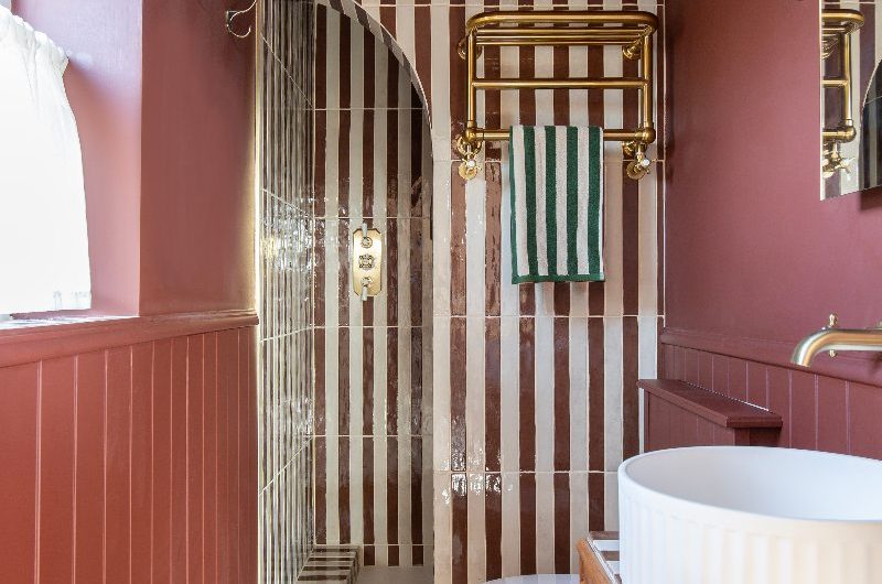 A burgundy design with a stripey shower area, grey hexagon tiles on the floor and a wood vanity unit with a fluted countertop basin.