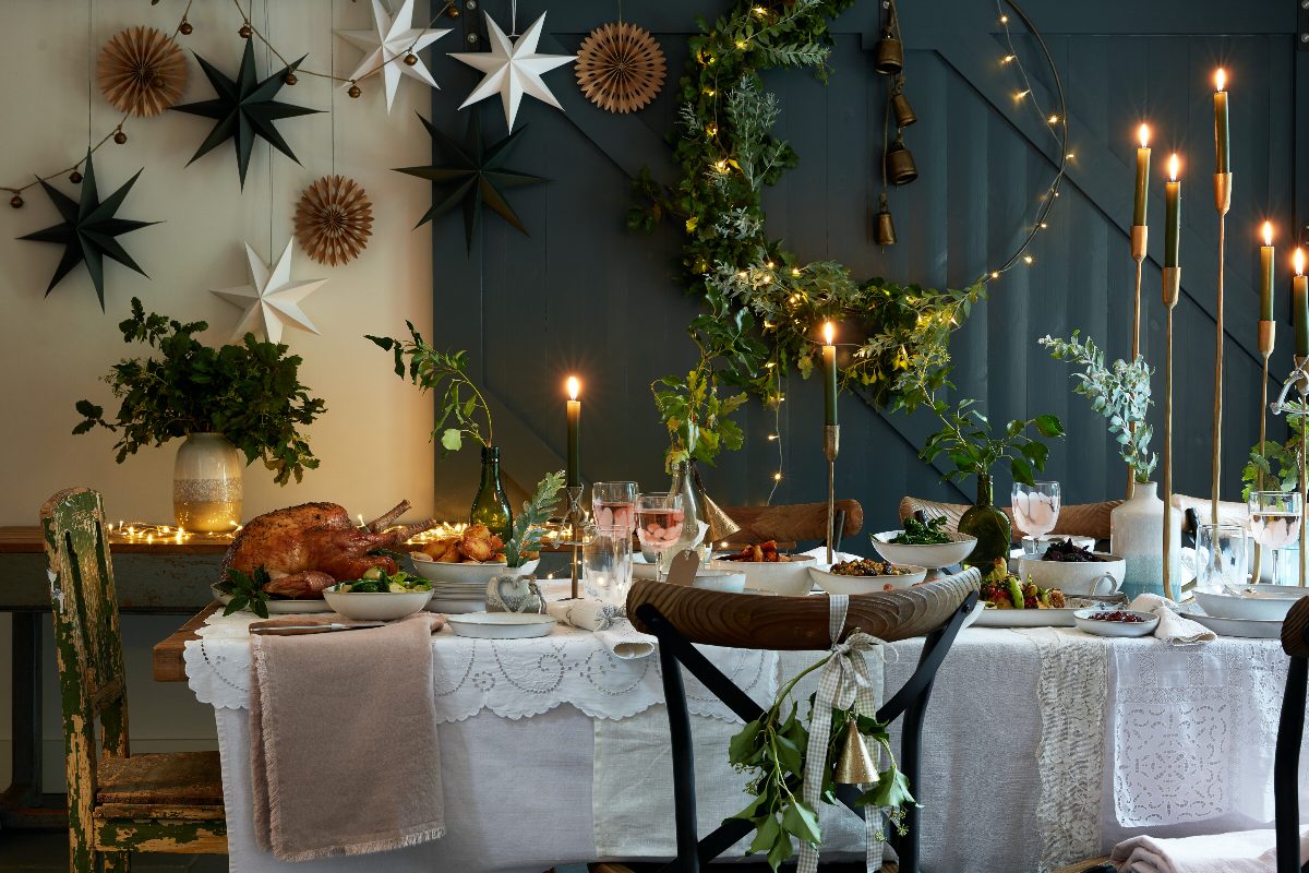 A festive dining room with a Christmas feast, a mix of candle sticks, paper decorations, and foliage.