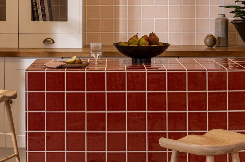 A country chic scheme with pink tiles on the wall, a glass cupboard, rustic decor and a central island tiled in dark red square slabs.