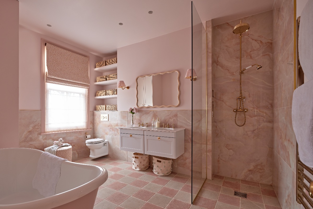 Bathroom drenched in pink with onyx tiles on the wall and checkerboard tiles on the floor, white wall-mounted toilet and double vanity unit, with a walk-in shower and a freestanding tub.