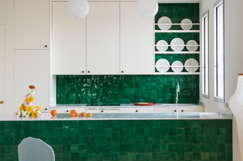 A kitchen design with white cabinets, a green tiled splashback, a peninsula with a matching tiled base and veiny work surfaces.
