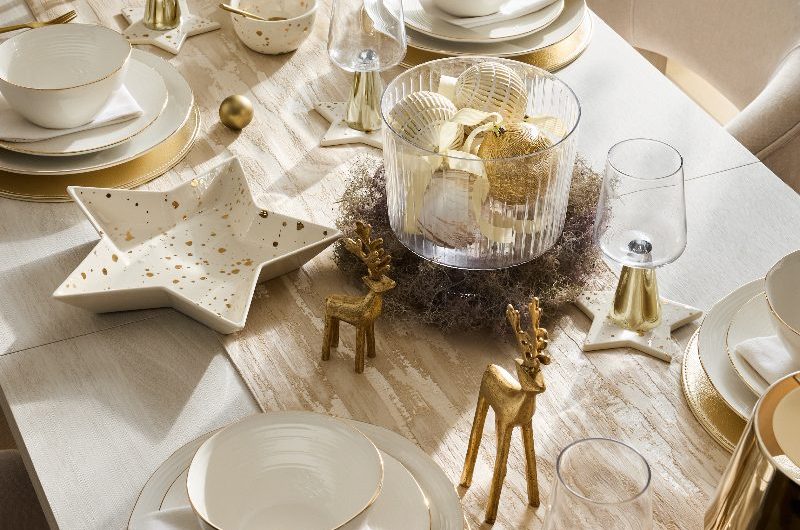 A simple table setup with white crockery with gold speckles and rims, gold decor and modern glassware.