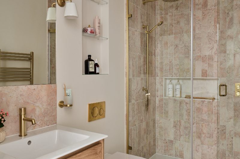 A neutral guest bathroom with a shower zone with light pink tiles, a wood vanity unit, and a wall-mounted toilet.