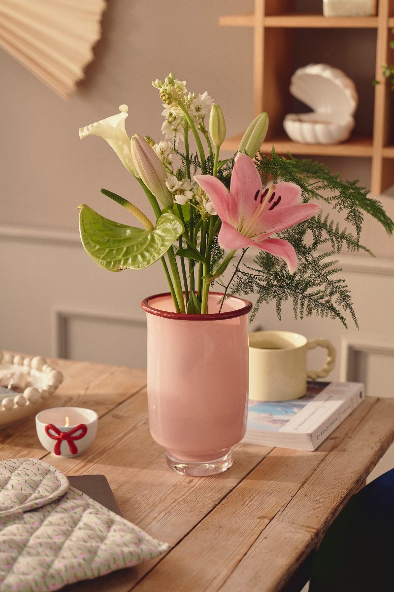 A pink vase on a wood table with spring flowers and minimalist homeware.