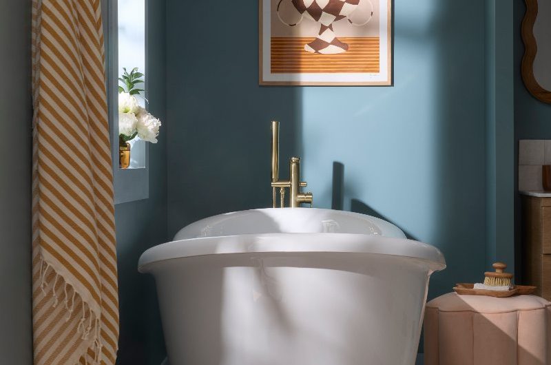 A colour drenched bathroom project with a freestanding tub, gold brassware, a frilled stool next to it, with patterned tiles on the floor.