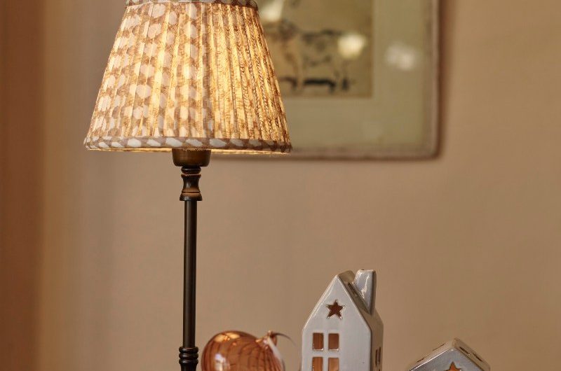 A wood side table with a table lamp, book, and ceramic lighthouses.