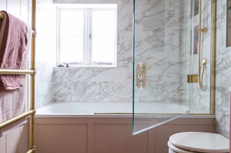 A light pink scheme with parquet flooring, classic sanitaryware, a fitted tub with a screen and marbled tiles.