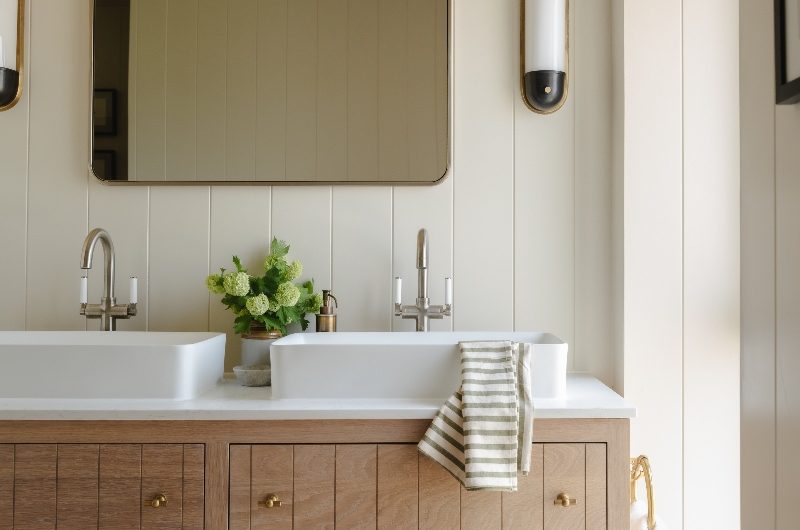 A calming bathroom in a countryside home with a double wood vanity unit, countertop basins, terracotta flooring and cream panelling.