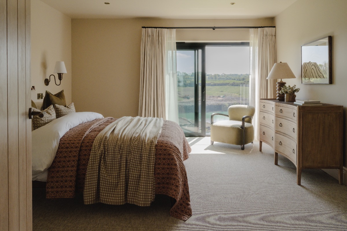 A bedroom design with neutral colours and gentle textures in the bedding, with a window overlooking the countryside landscape.