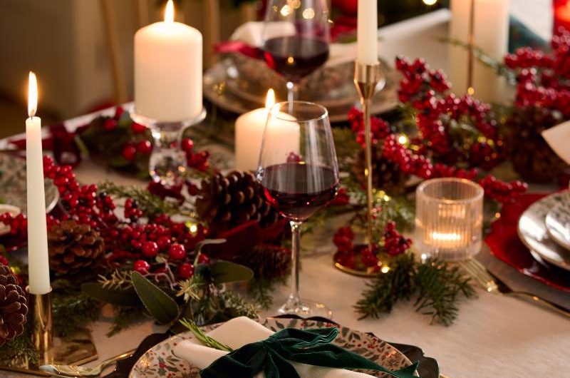 Classic Christmas scheme with red holly berries and pinecone garlands, red and green charger plates, and simple glassware.