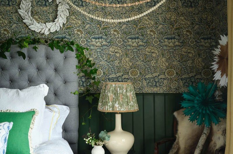 A colourful bedroom design with patterned wallpaper, wall panelling, an upholstered bed, and green furnishings.