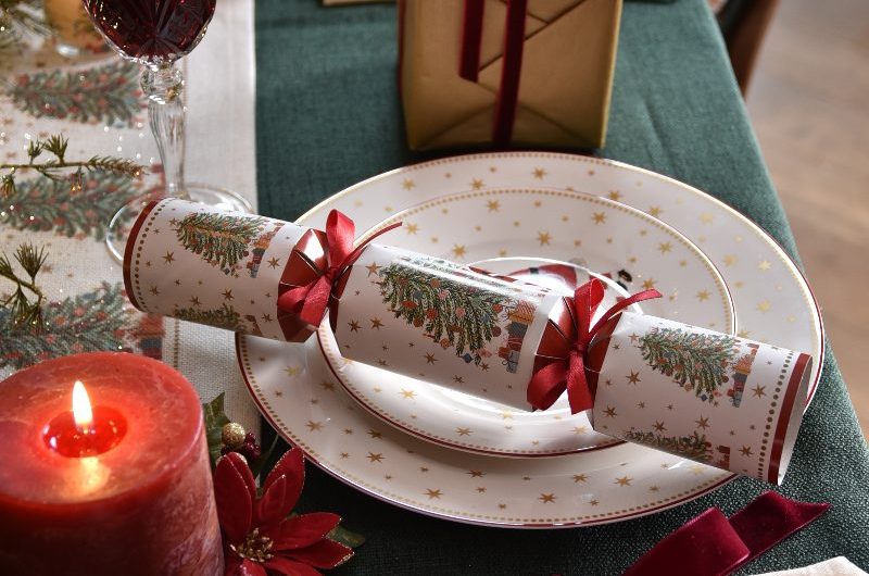 A classic Christmas tablescheme with star patterned white dinner set, gold cutlery tied up with ribbons, and festive crackers.