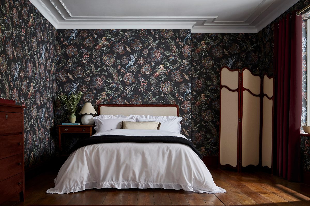 Calm bedroom design with moody wallpaper, wood furniture, wood flooring, and white bed linen.