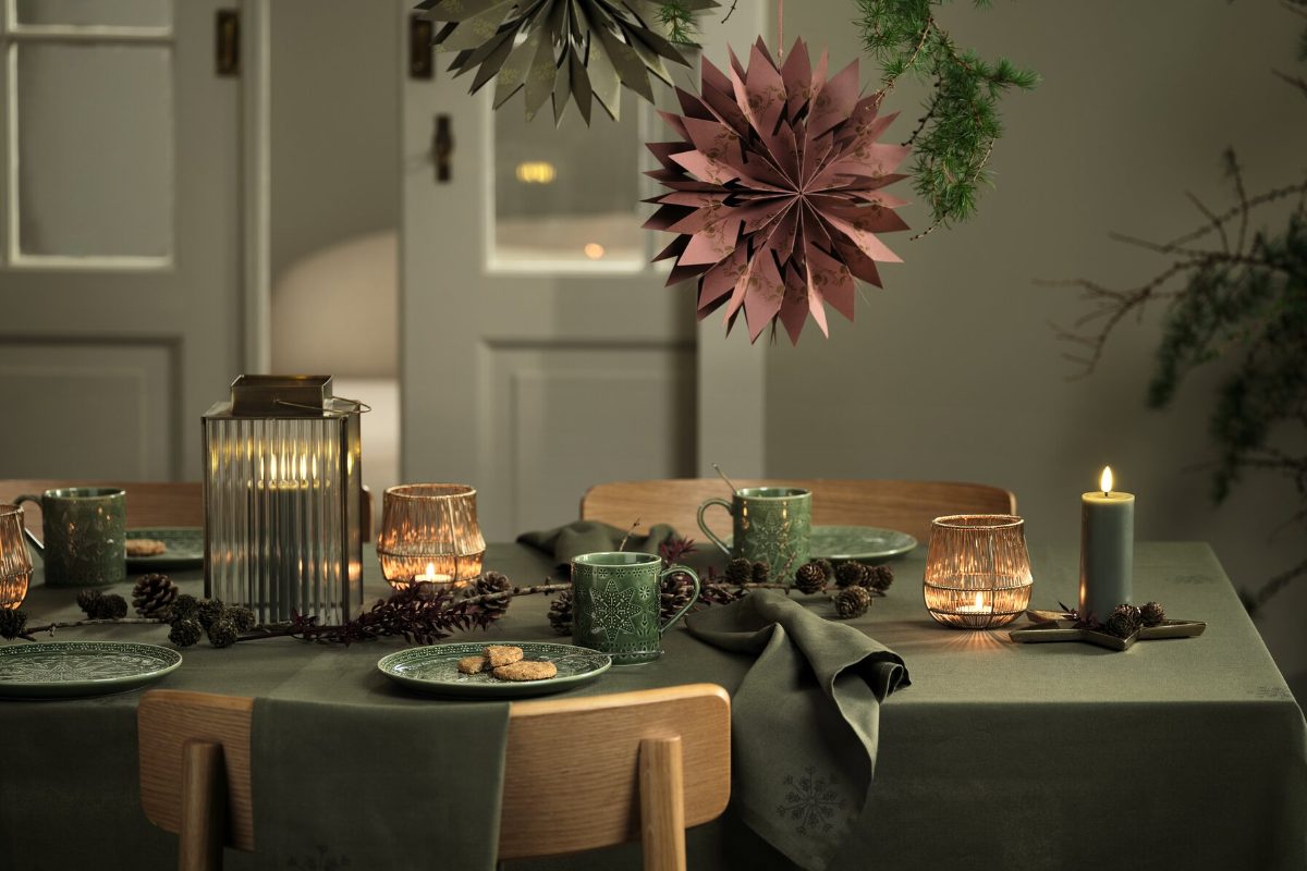 A simple, green Scandi scheme with glass lanterns, hanging paper decorations, and wood chairs.