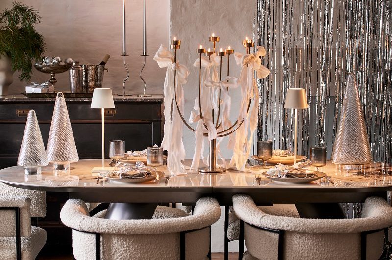 A modern and minimalist table setup with glass tree decor, a large candle holder, and frosted glassware. 