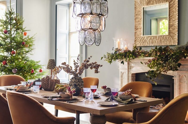 A simple, chic dining room with mustard velvet chairs, a wood table, glass chandelier, and a fireplace.