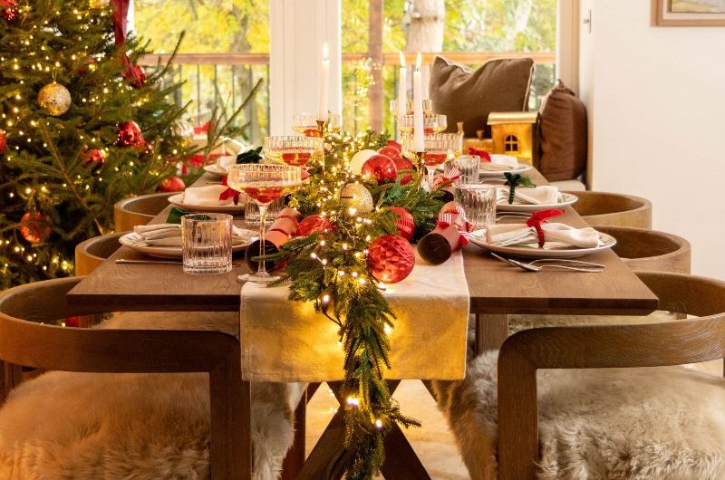 Festive dining room with a wood table, chairs with faux fur seats, and a tree in the corner.