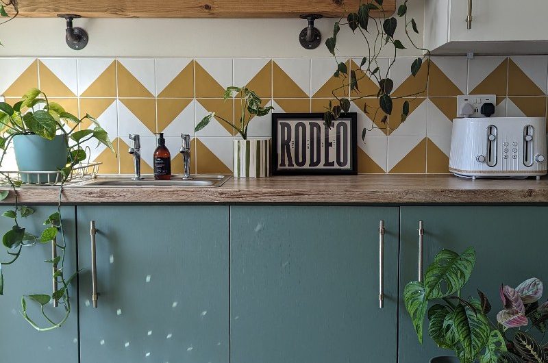 A colourful kitchen renovation with green units, wood worktops, wood shelving and patterned tiles.