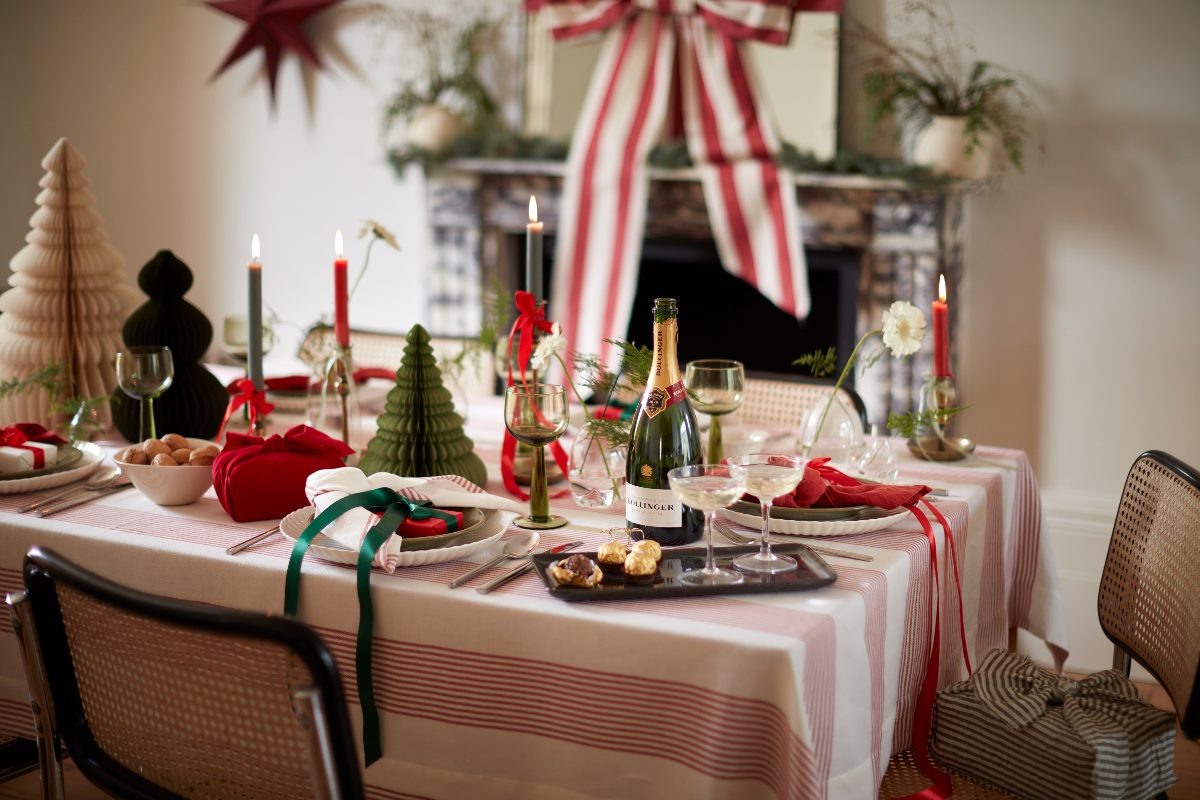 A festive tablescape with paper trees, striped tablecloth, red and green candles, and an oversized bow in above the fireplace mirror.