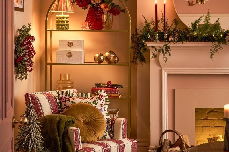 A cosy living room with a striped armchair, fireplace, metal bookshelf, and green reeded side table, with a checkered rug on the floor.
