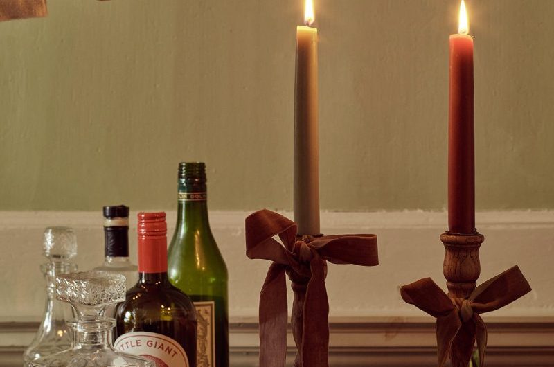A bar area with two lit candles on wood sticks, tied with ribbon, and a brass snuffer.