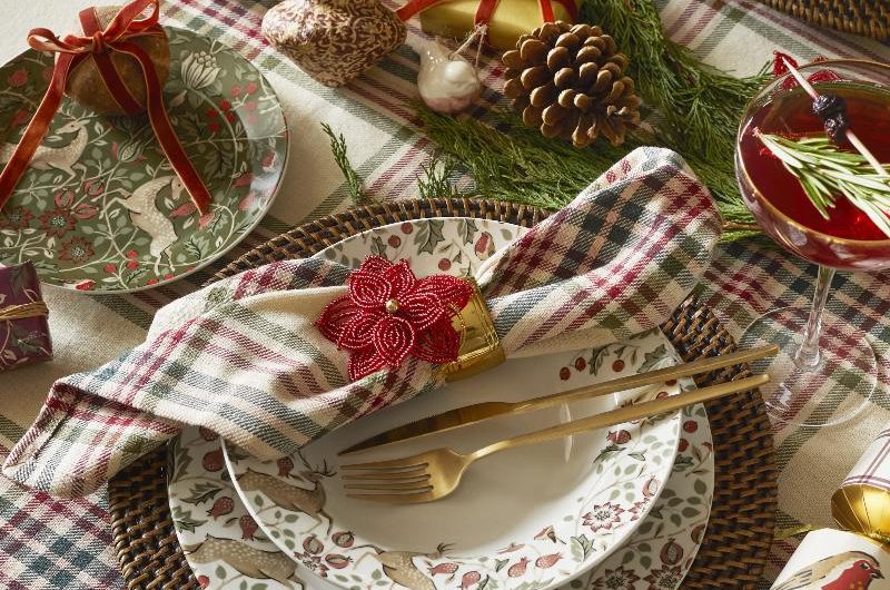 A classic Christmas tablescape with plaid tablecloth, matching napkins, rattan charger plates, floral dinner set, and green foliage.