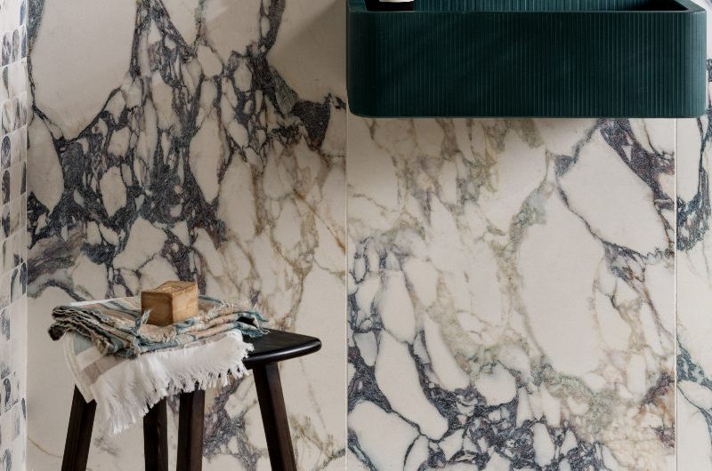 A bathroom design with large formal  porcelain wall tiles with a veiny pattern and a wall-mounted blue basin with nickel brassware.