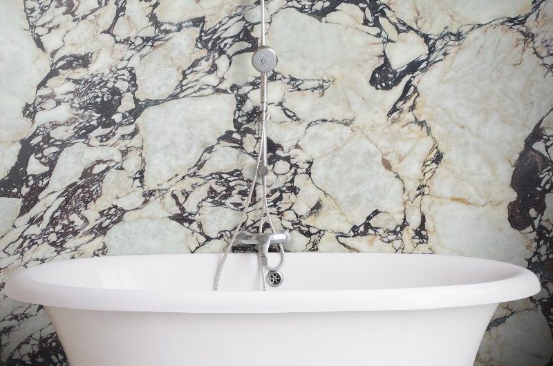 A glamorous bathroom with square marble tiles on the floor, a freestanding tub with feet, and a large Calacatta Viola marble slab on the wall behind it.