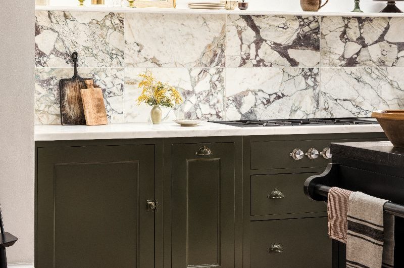 A kitchen design with green Shaker units, marble tiles on the cooking run, an open shelf for decor, checkerboard flooring, and an island.