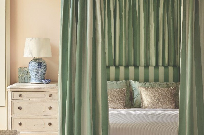 A Rococo style bedroom interior design with a pour poster bed clad in striped fabrics, with vintage furniture and and blush pink walls.