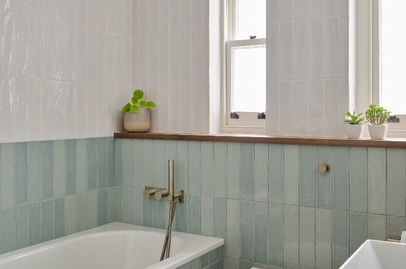 A calm bathroom with light blue metro tiles on the bottom half of the wall and fitted tub, and white metro tiles on the upper half of the wall.